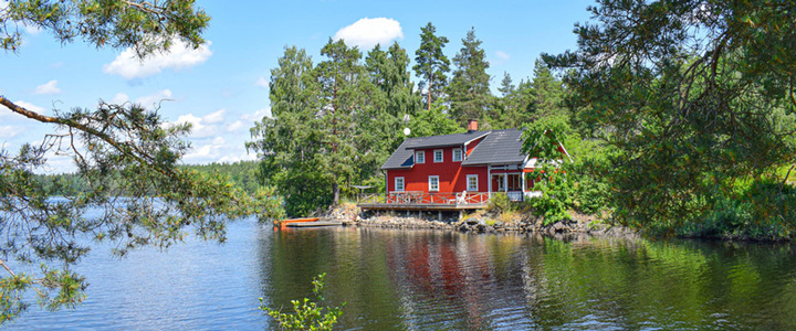 Großzügiges rotes Ferienhaus mitten in der sommerlichen unberührten Natur, direkt am klaren Wasser gelegen.
